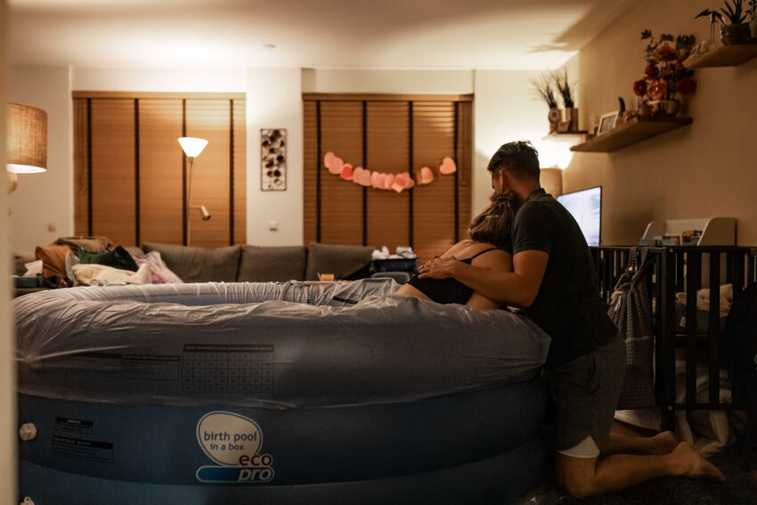 Geboortefotografie in Heemskerk legt een thuisbevalling midden in de nacht vast, moeder zit in een bevalbad en vangt haar weeën op.