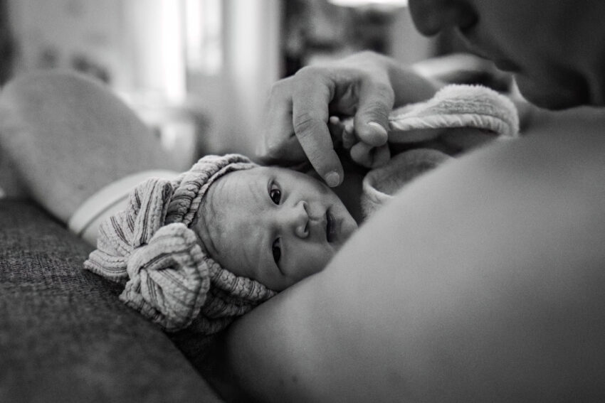 pasgboren dochter ligt met haar ogen wijd open in de armen van haar vader bij een thuisbevalling