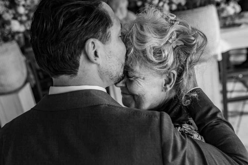Echte momenten tijdens trouwfotografie, bruidegom kust zijn moeder op haar voorhoofd
