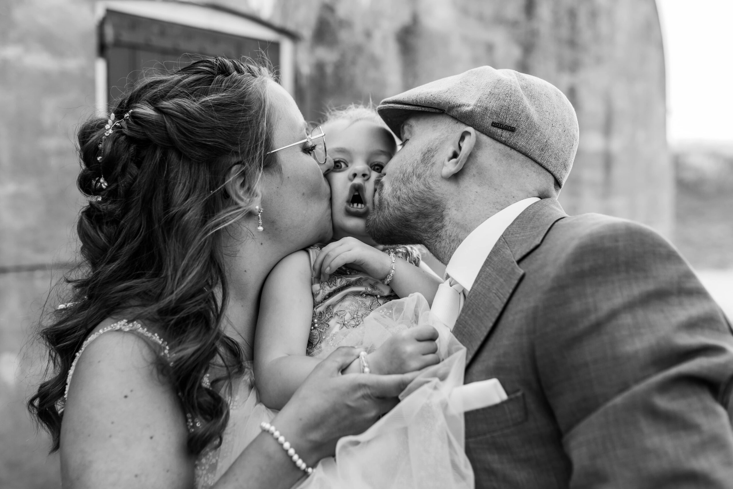 Bruidspaar kussend met hun dochter, dochter trekt een grappig gezicht.