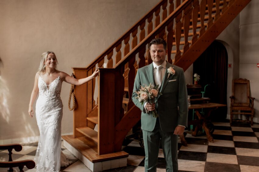 Trouwfotograaf in Kasteel Dussen, de bruidegom wacht gespannen tot hij zijn bruid voor het eerst ziet. De bruid loopt net van de trap af naar beneden.