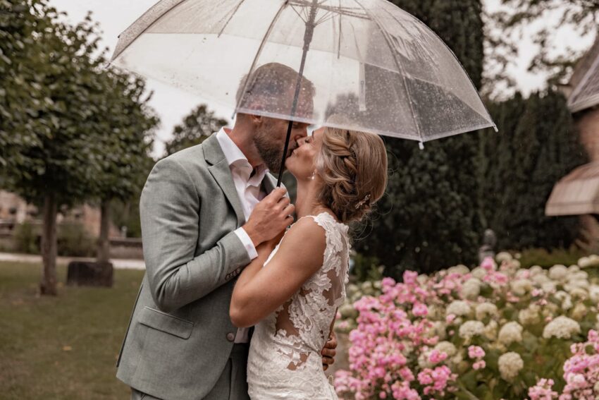 trouwfotograaf maakt foto's van bruidspaar in de regen onder een doorzichtige paraplu